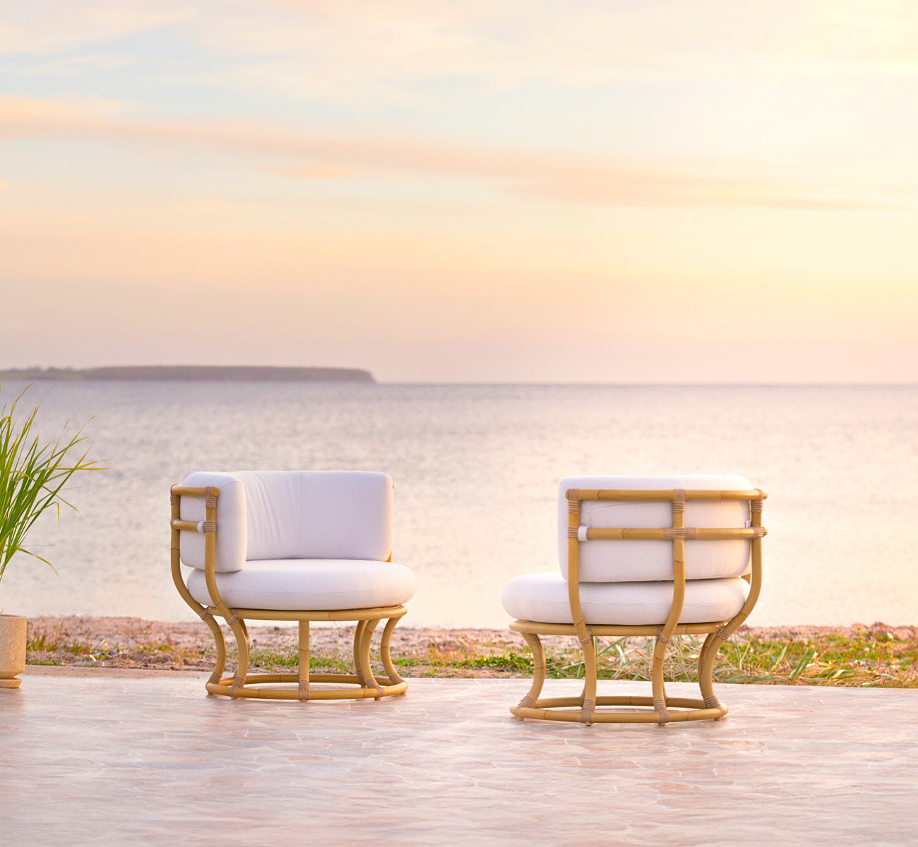 This is a lifestyle image of Coco Exterior Lounge Chair in natural Aluminium ArtFibre, on an open coastal terrace at sunset with sea views.