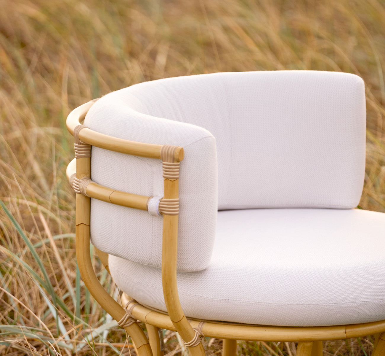 This is a lifestyle image of Coco Exterior Lounge Chair in natural Aluminium ArtFibre, on an open coastal terrace at sunset with sea views.