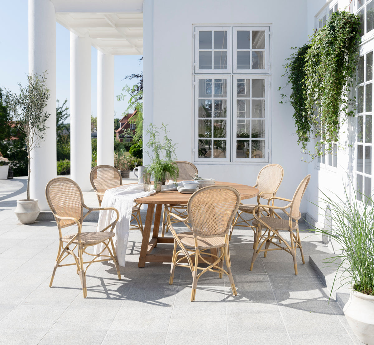 This is a lifestyle image of Rossini Exterior Dining Armchair in natural aluminium artfibre. Styled in a bright interior setting.