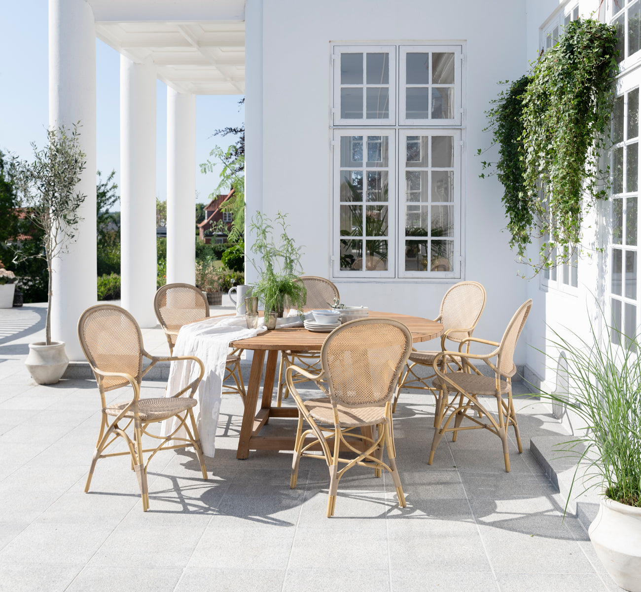 This is a lifestyle image of Rossini Exterior Dining Armchair in natural aluminium artfibre. Styled in a bright interior setting.
