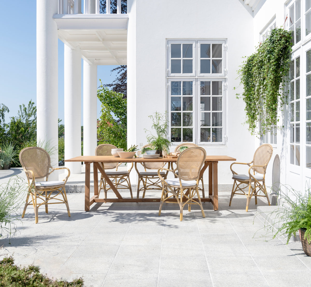 This is a lifestyle image of Rossini Exterior Dining Armchair in natural aluminium artfibre. Styled in a bright interior setting.