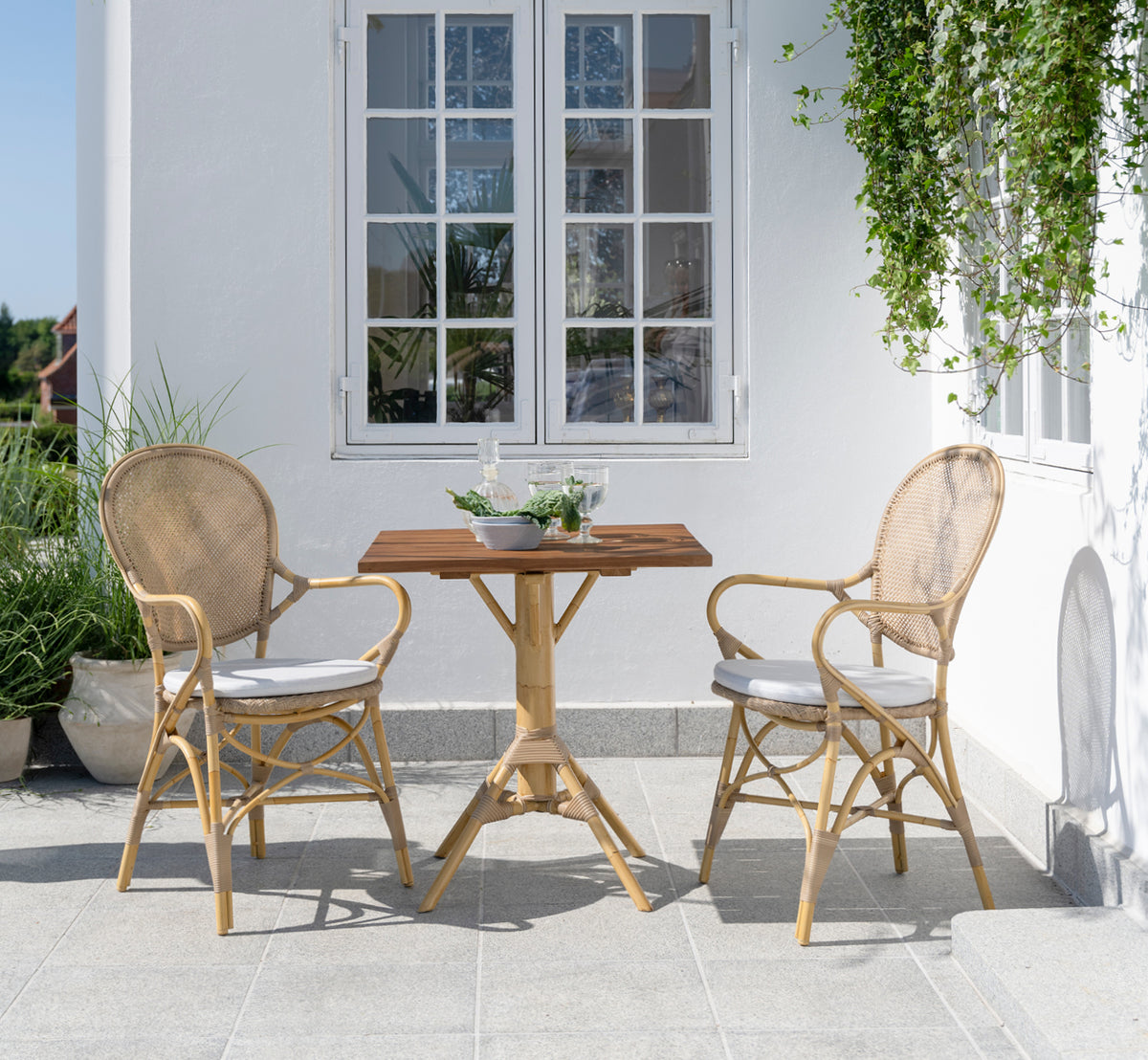 This is a lifestyle image of Rossini Exterior Dining Armchair in natural aluminium artfibre. Styled in a bright interior setting.
