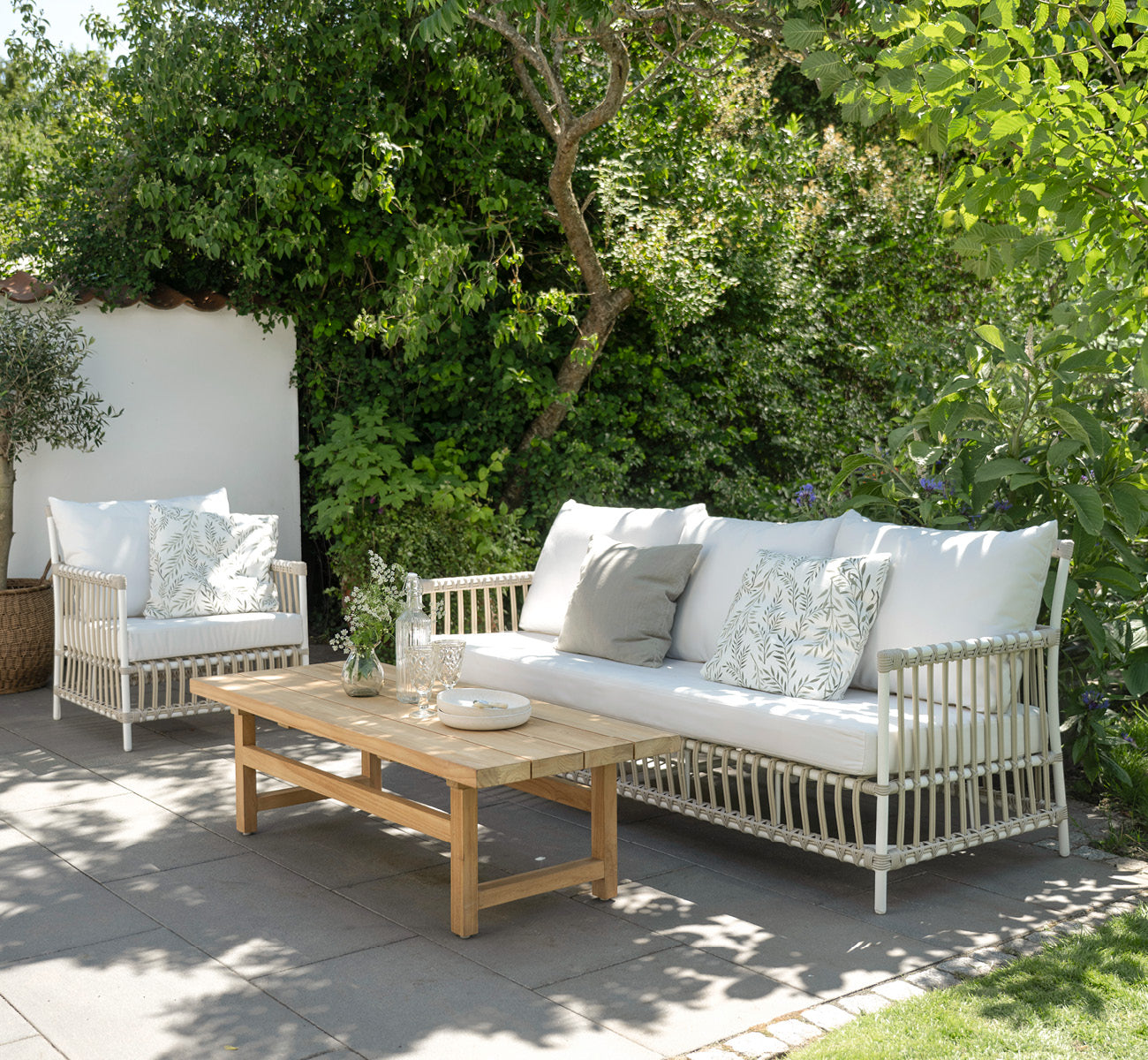 This is a lifestyle image of Caroline Exterior Lounge Chair in dove White Aluminium ArtFibre, on a waterside wooden deck with coastal greenery and.