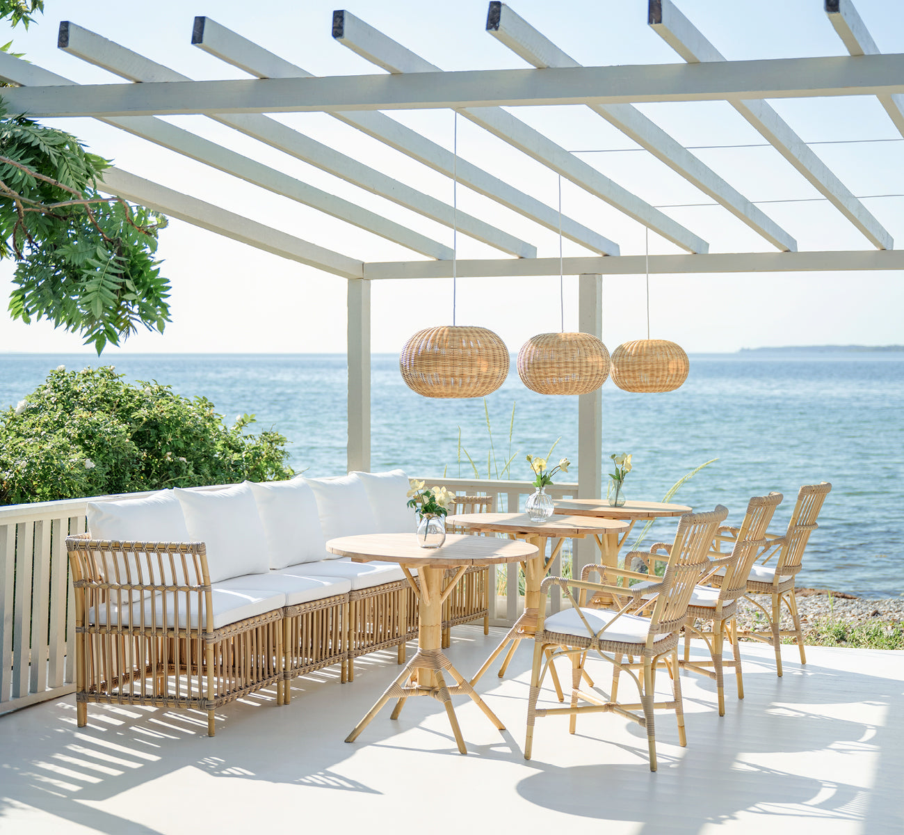 This is a lifestyle image of Meghan Exterior Dining Bench Center Module in natural aluminium artfibre. On a seaside pergola deck.