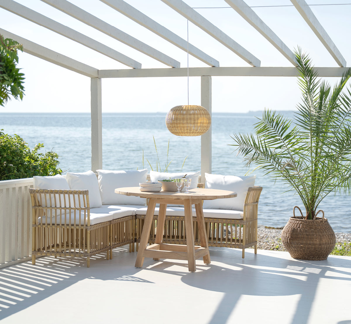 This is a lifestyle image of Meghan Exterior Dining Bench Center Module in natural aluminium artfibre. Around a round seaside table.
