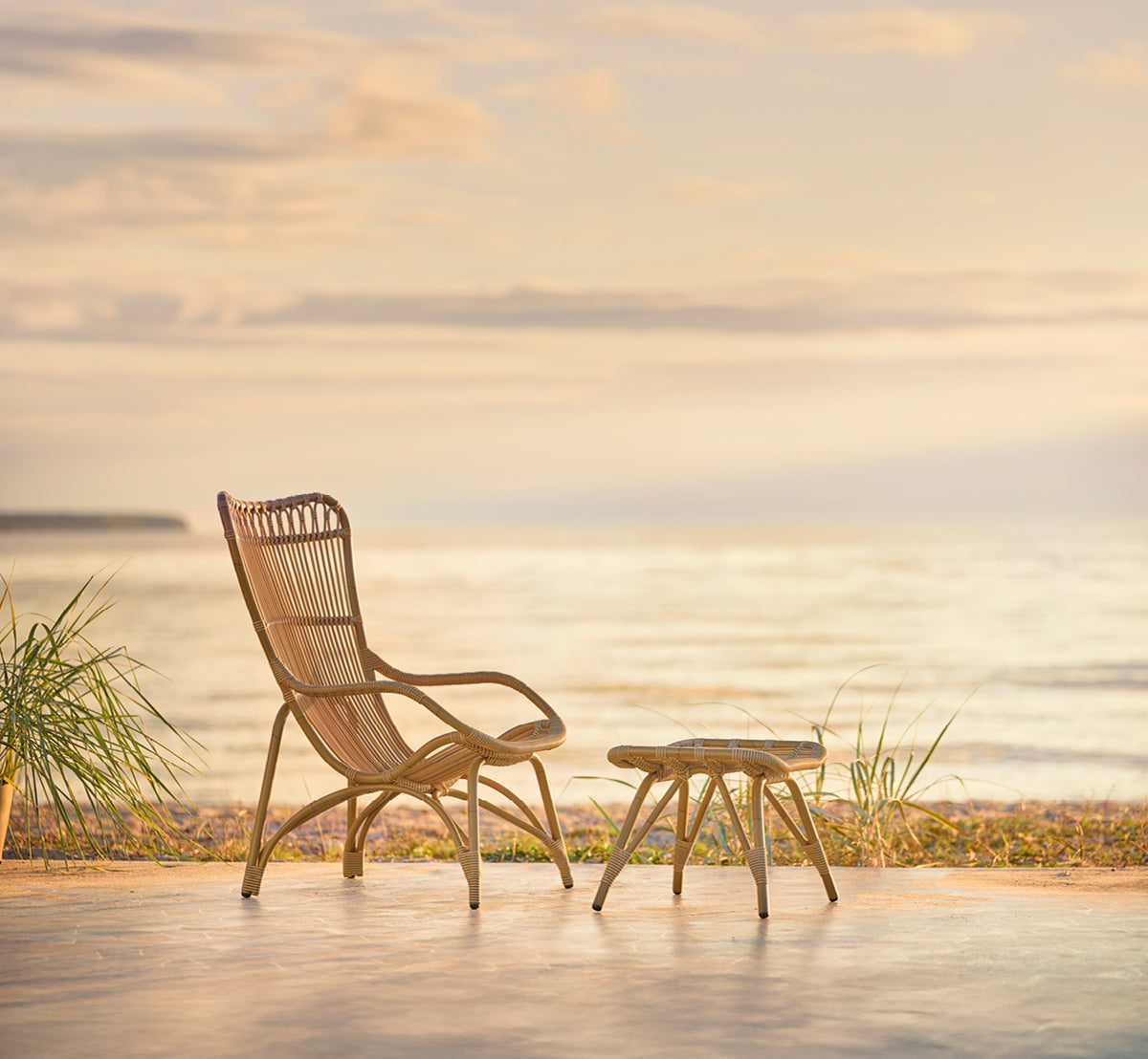This is a lifestyle image of Monet Exterior Lounge Chair in antique aluminium artfibre. On a beach pavilion with white curtains.