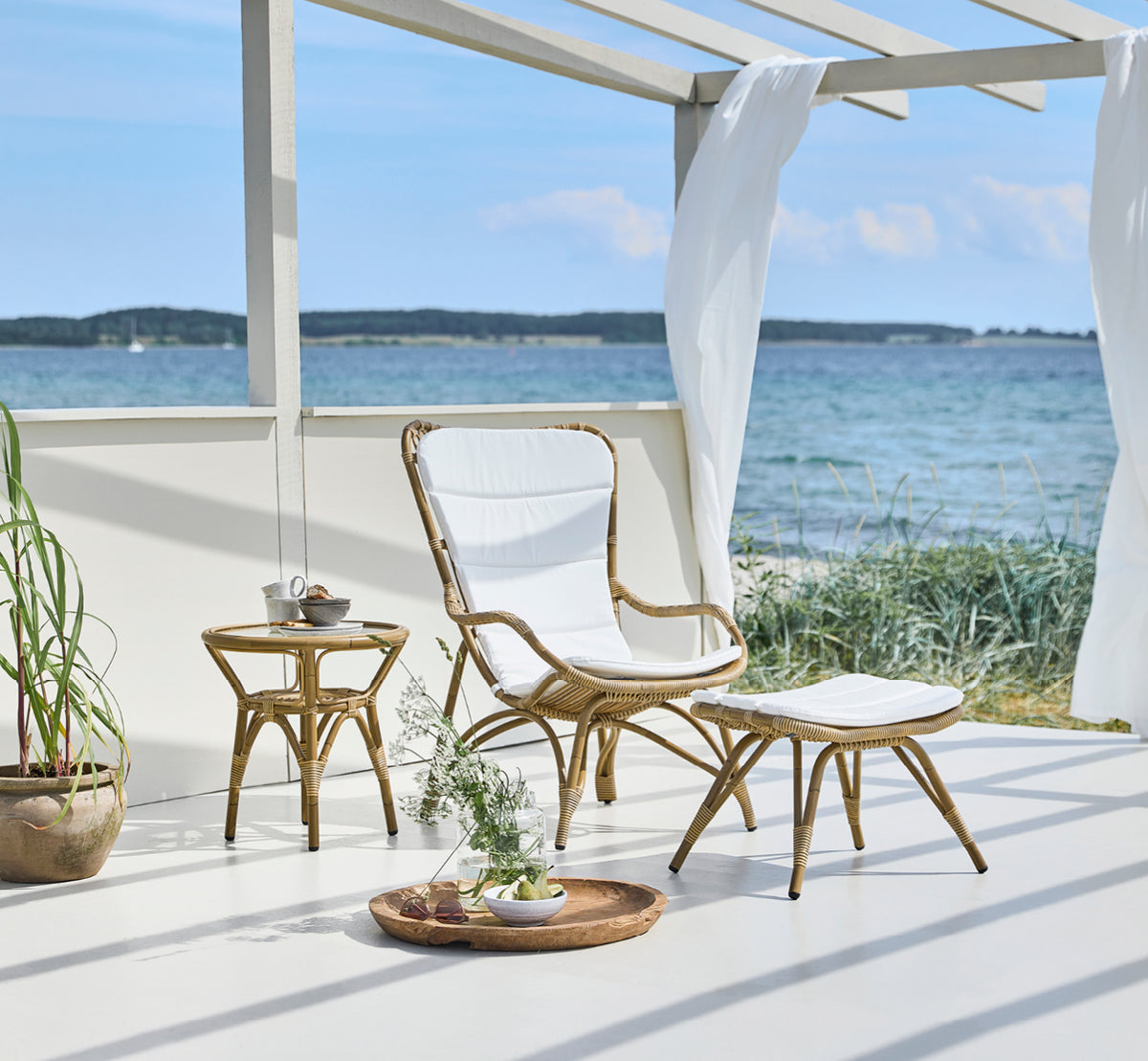 This is a lifestyle image of Monet Exterior Lounge Chair in antique aluminium artfibre. With footstool on a seaside pavilion deck.