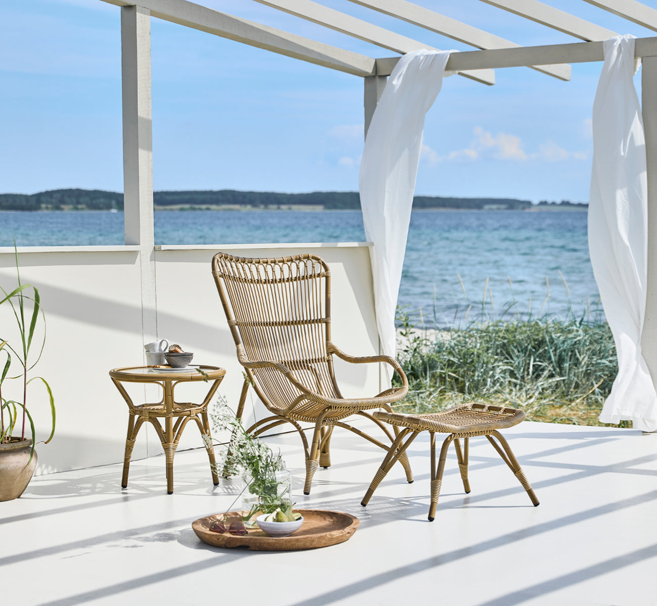 This is a lifestyle image of Monet Exterior Lounge Chair in antique aluminium artfibre. With footstool on a beach deck with sea view.