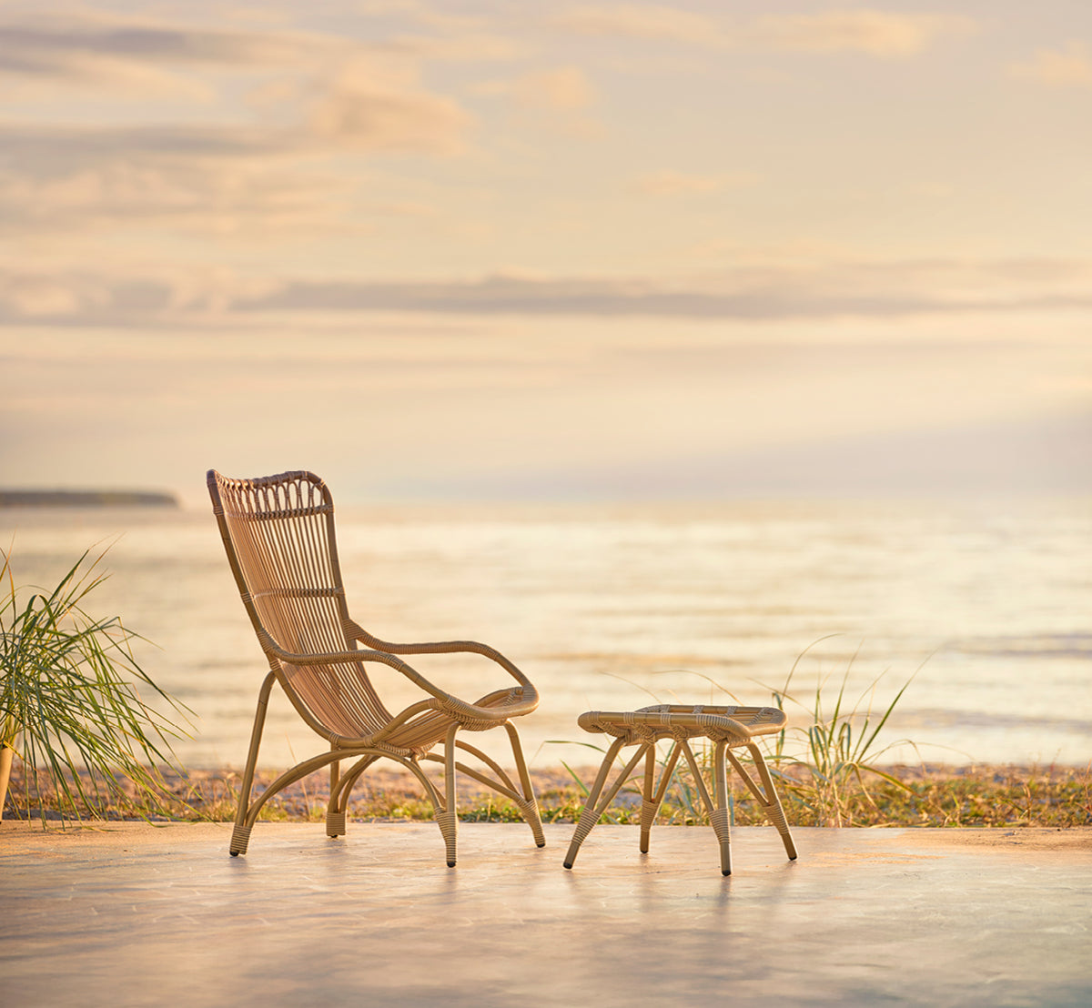 This is a lifestyle image of Monet Exterior Footstool in antique aluminium artfibre. With lounge chair on a beach pavilion deck.