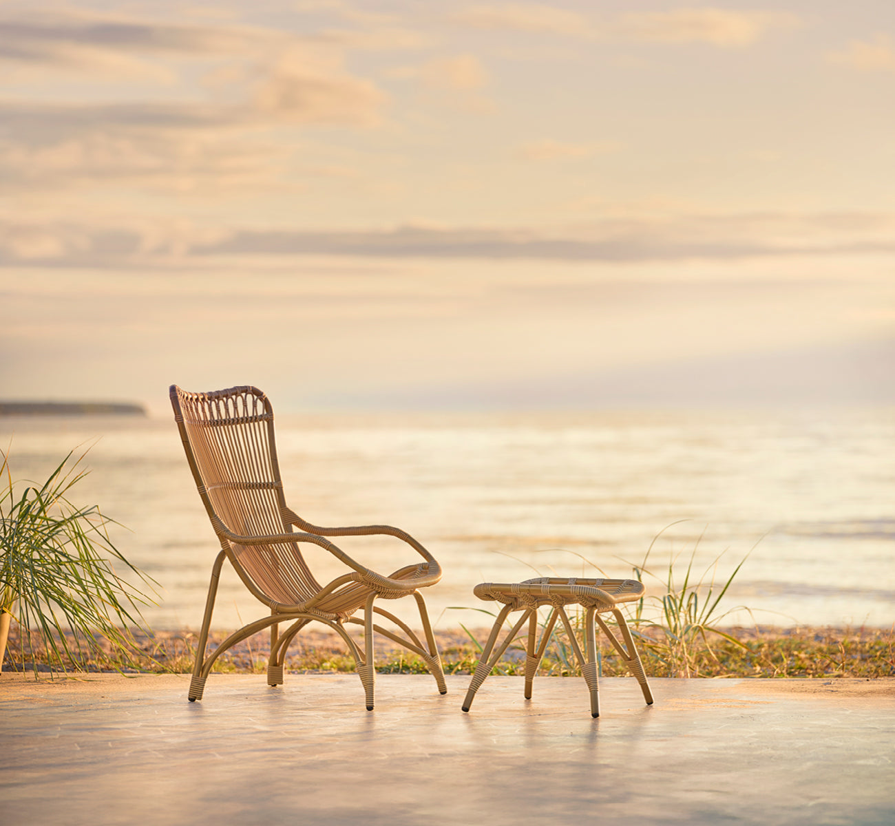 This is a lifestyle image of Monet Exterior Footstool in antique aluminium artfibre. With lounge chair on a beach pavilion deck.