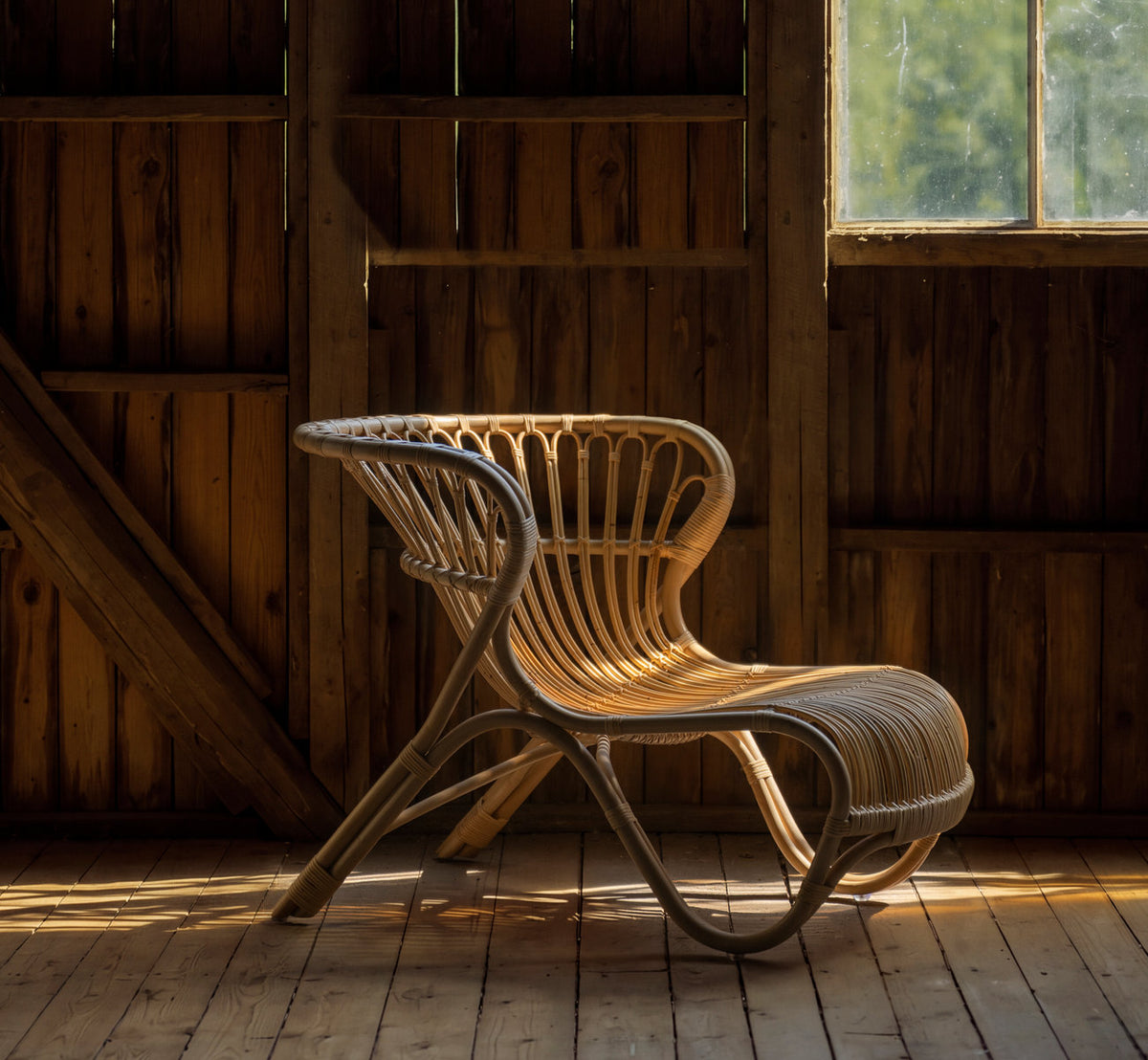 This is a lifestyle image of Fox Lounge Chair in polished natural rattan. In a wooden barn with warm window light.