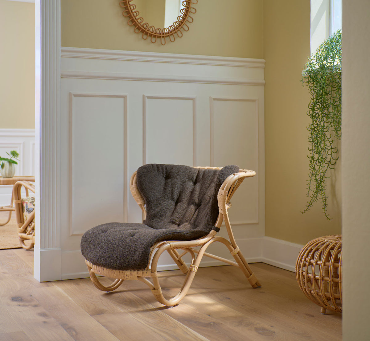 This is a lifestyle image of Fox Lounge Chair in polished natural rattan. With grey cushion by white panels.