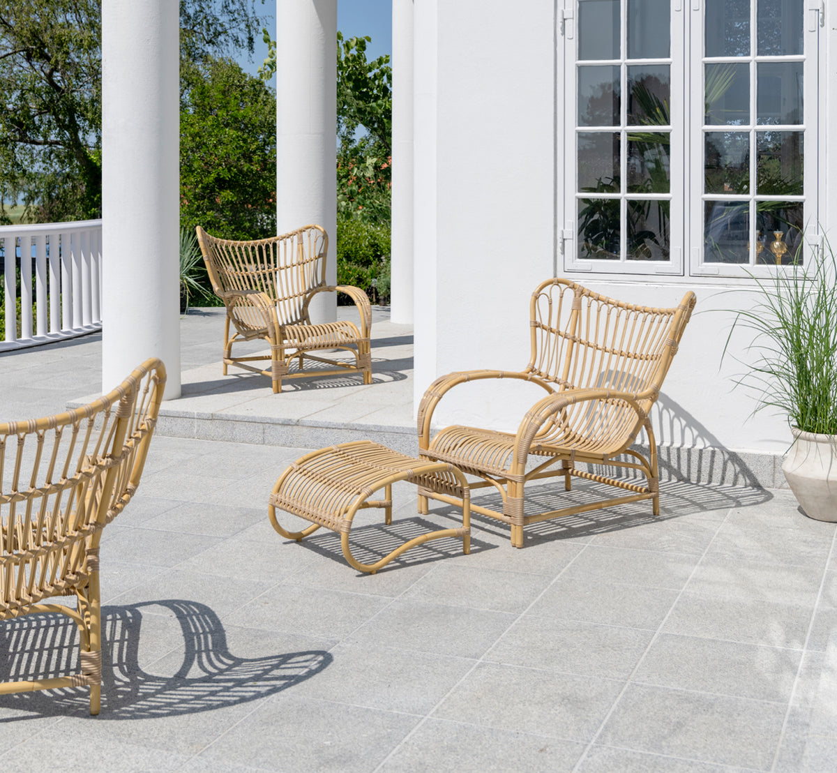This is a lifestyle image of Teddy Exterior Lounge Chair in natural aluminium artfibre. Placed on a sunny paved terrace by a white-framed doorway.