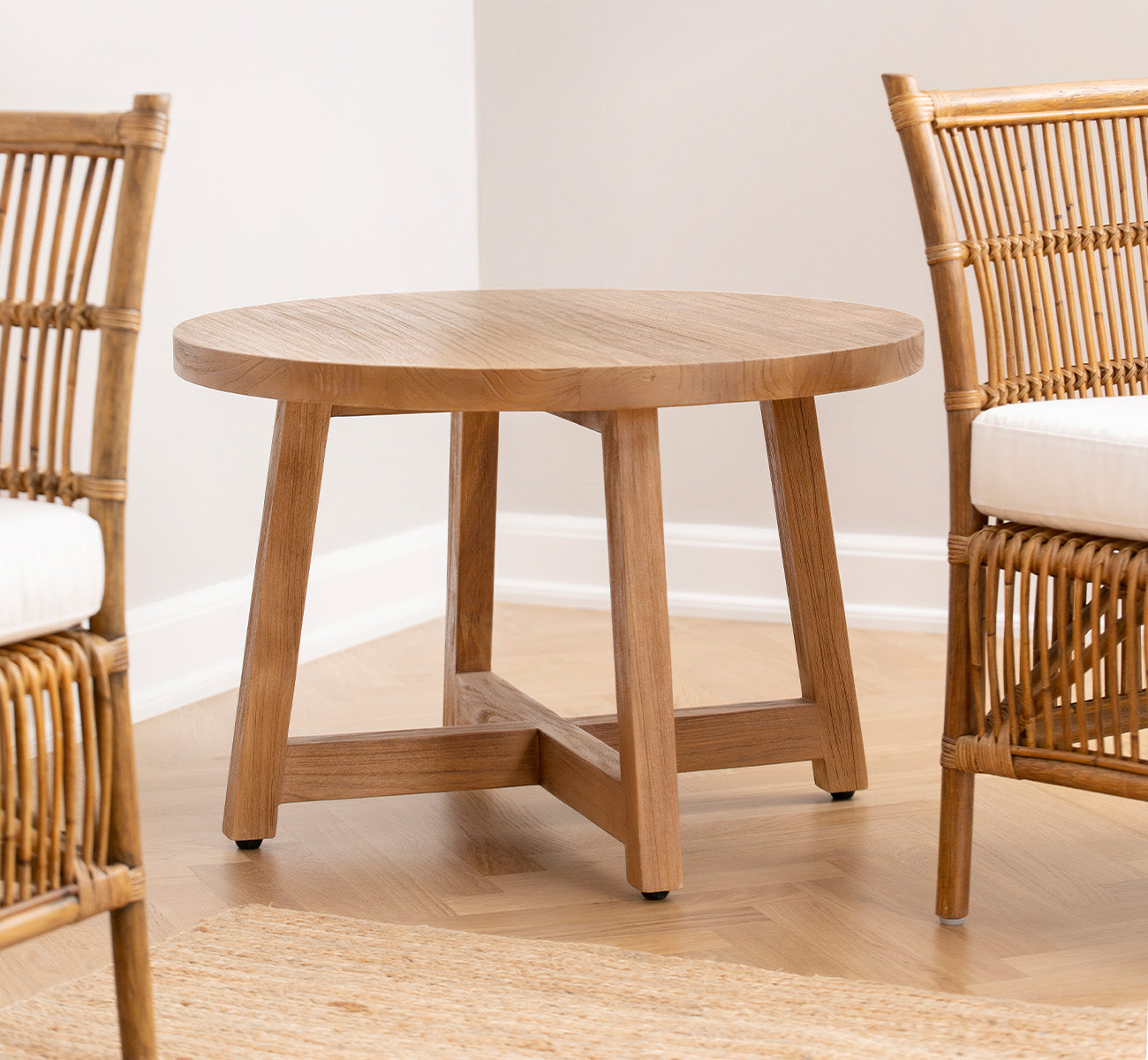 This is a lifestyle image of Aksel Coffee Table in teak indoor, in a bright interior with herringbone parquet and rattan chairs.