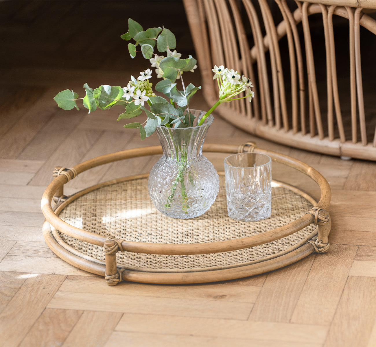 This is a lifestyle image of Andreas Tray in natural Rattan, in a bright interior with herringbone parquet flooring.