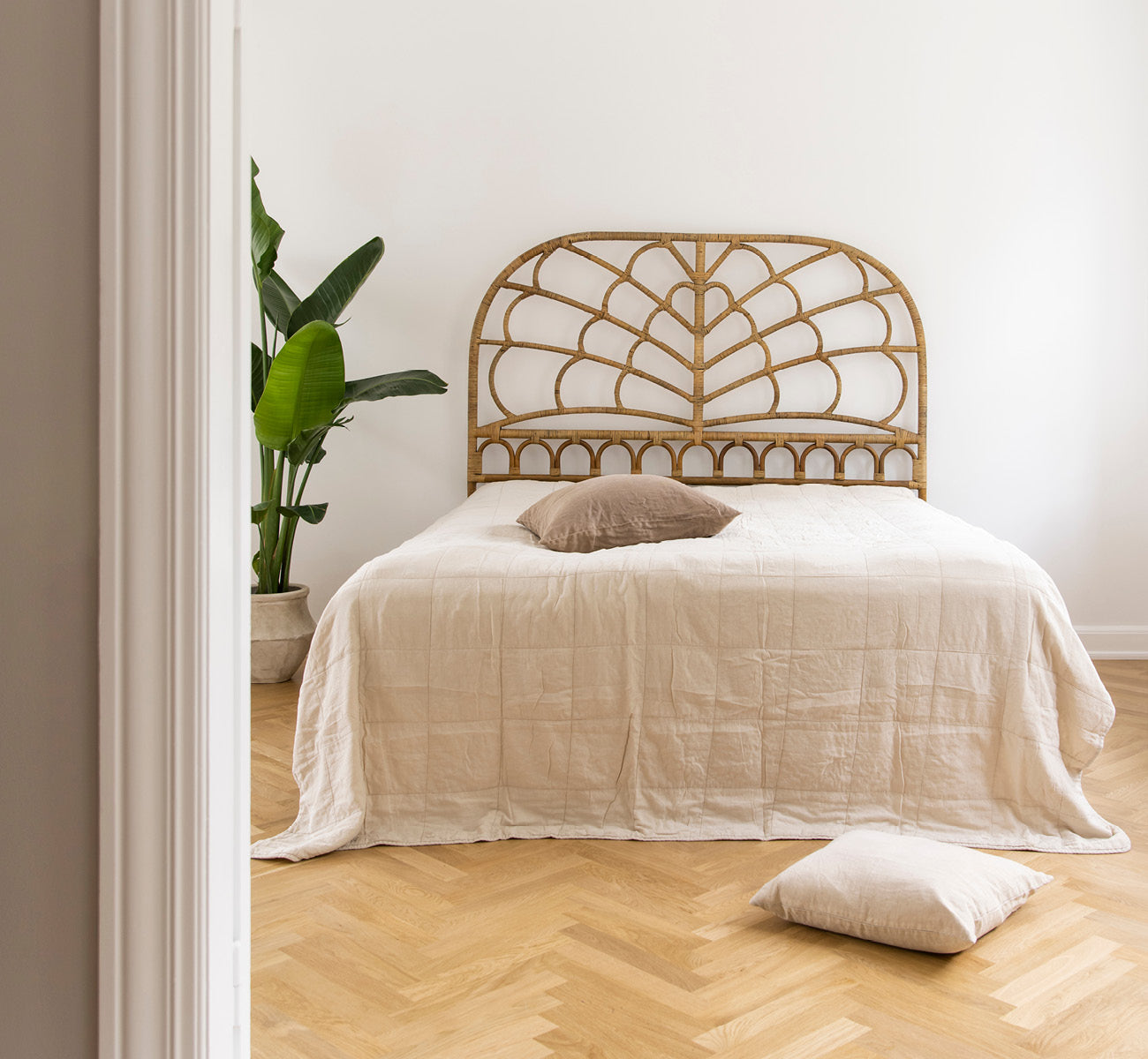 This is a lifestyle image of Celia Headboard in antique rattan, in a serene bright bedroom with neutral linen and herringbone parquet.