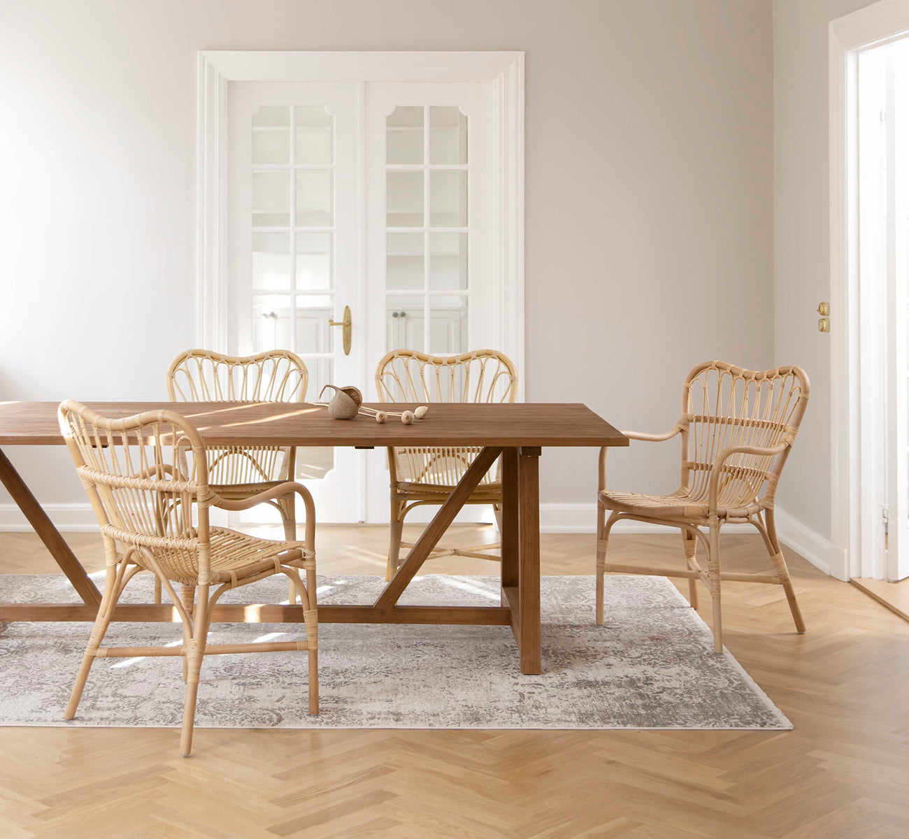 This is a lifestyle image of Margret Dining Chair in natural rattan. Placed around a teak dining table in a bright Scandinavian room with oak floors.