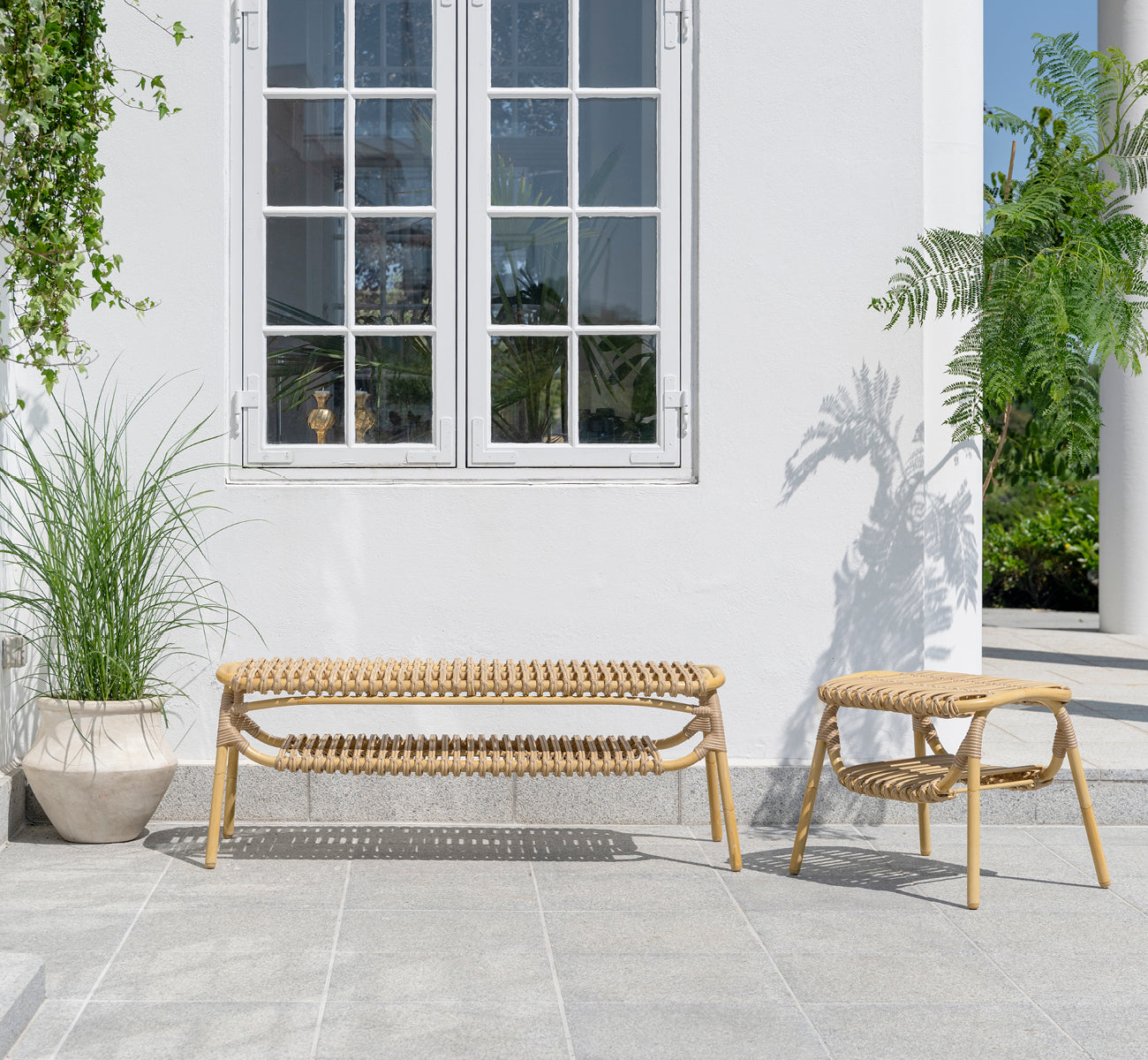 This is a lifestyle image of Machiya Exterior Bench in natural aluminium artfibre. White patio with exterior stool and green plants.