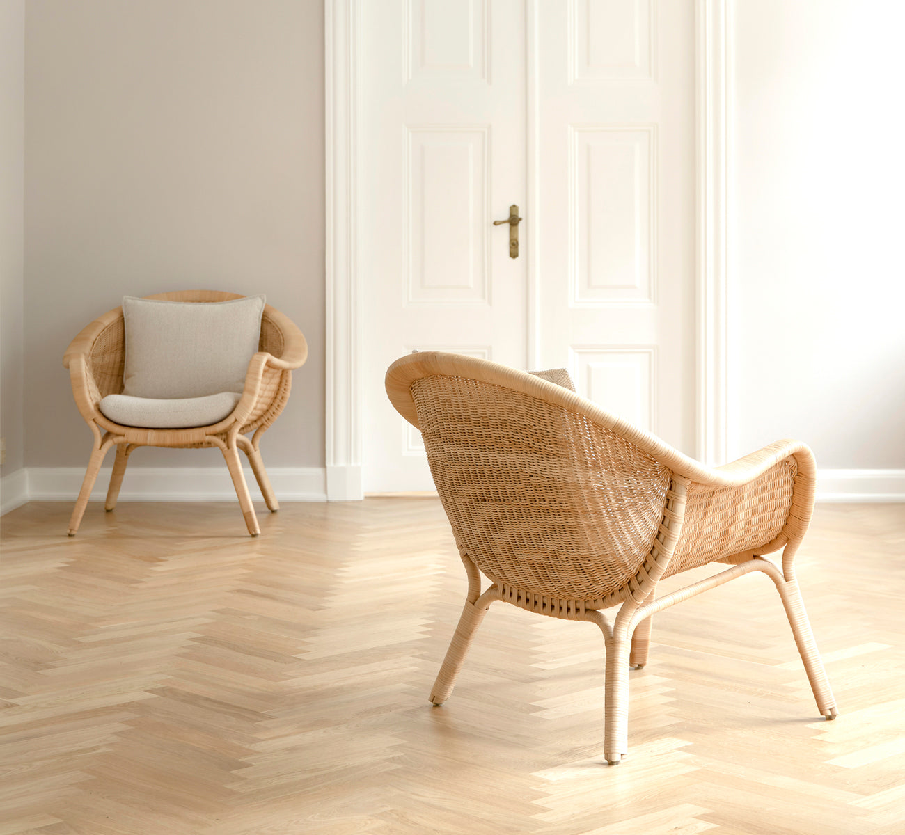 This is a lifestyle image of Madame Lounge Chair in natural core weave rattan frame. Bright room with herringbone floor and white double doors.