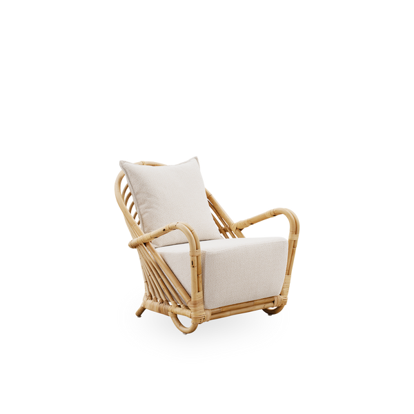 Side view of the Charlottenborg Lounge Chair in polished natural rattan, designed by Arne Jacobsen. The chair features a curved back and armrests integrated into the base, handcrafted from high quality Indonesian rattan.