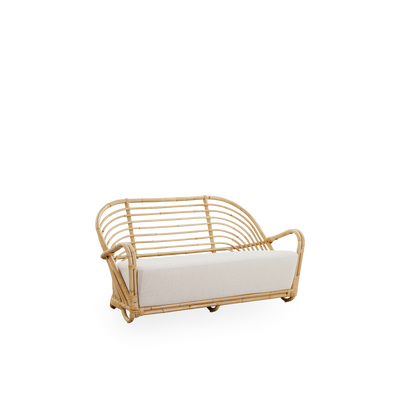 Side view of the Charlottenborg 2-seater Sofa in polished natural rattan, designed by Arne Jacobsen. The sofa features a curved back and armrests integrated into the base, handcrafted from high quality Indonesian rattan.