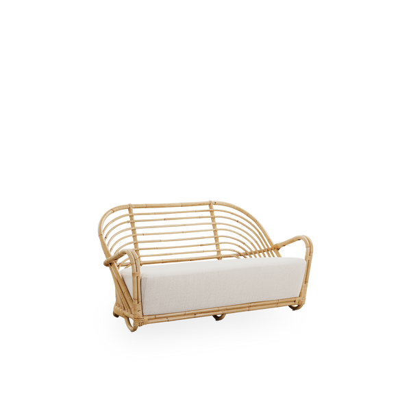 Side view of the Charlottenborg 2-seater Sofa in polished natural rattan, designed by Arne Jacobsen. The sofa features a curved back and armrests integrated into the base, handcrafted from high quality Indonesian rattan.