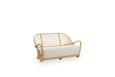 Side view of the Charlottenborg 2-seater Sofa in polished natural rattan, designed by Arne Jacobsen. The sofa features a curved back and armrests integrated into the base, handcrafted from high quality Indonesian rattan.