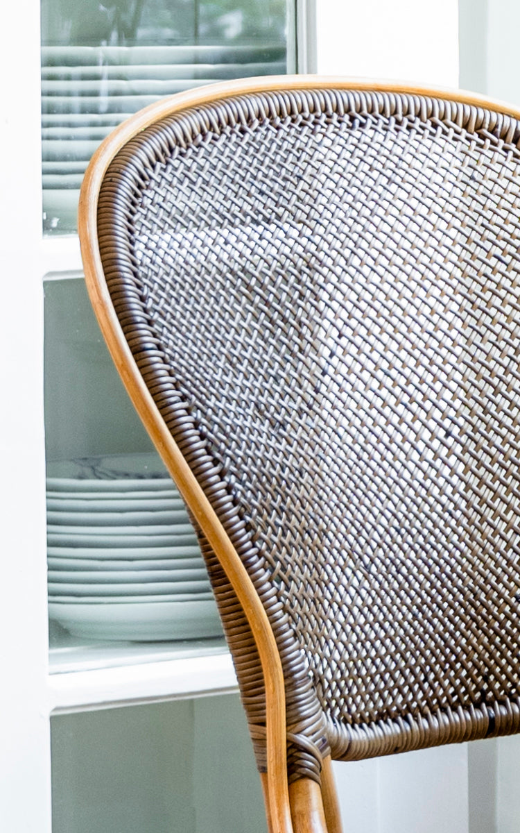 This is a close-up image of Rossini Dining Chair in cherry rattan. Detailed view of the dark cherry cane weave backrest against light cabinetry.