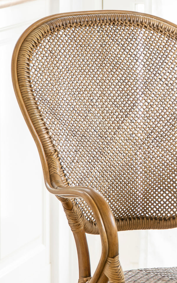 This is a close-up image of Rossini Dining Armchair in antique rattan. Detail of the curved rattan armrest, woven seat and wrapped joints.