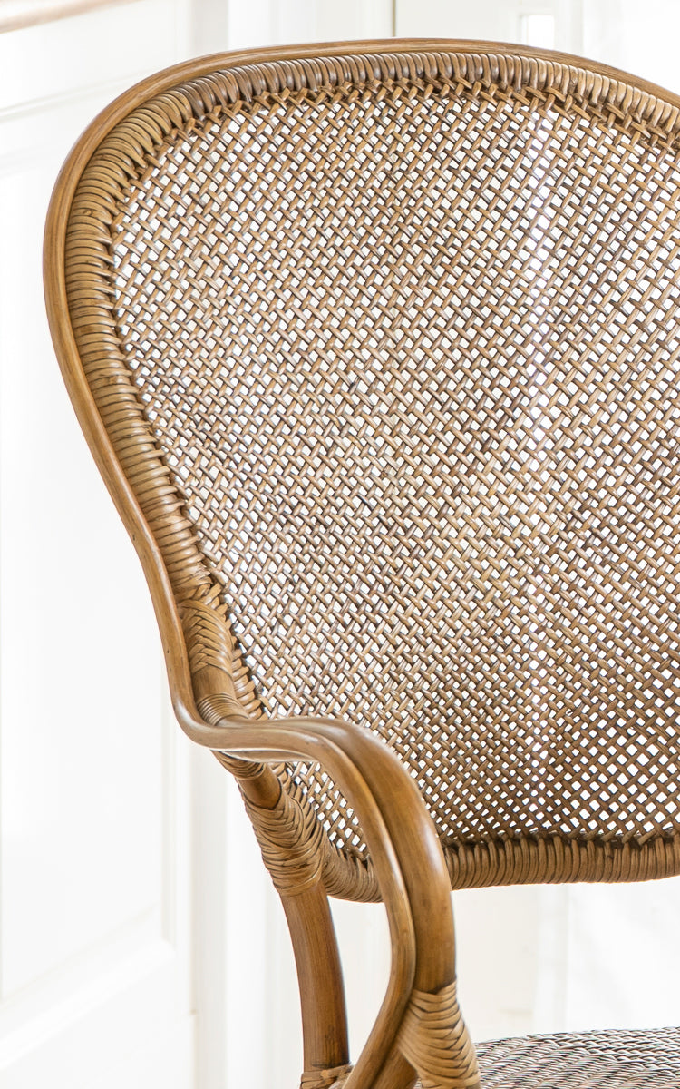 This is a close-up image of Rossini Dining Armchair in antique rattan. Detail of the curved rattan armrest, woven seat and wrapped joints.