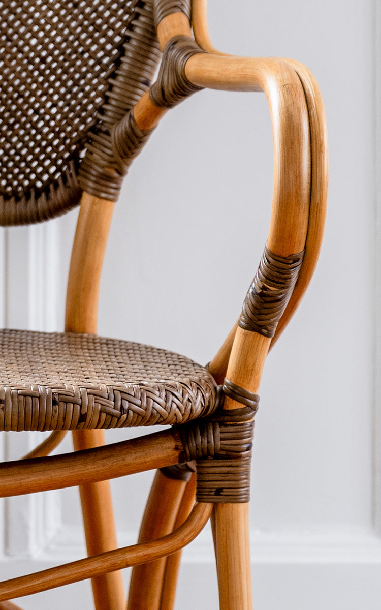 This is a close-up image of Rossini Armchair in cherry rattan. Two-tone cherry cane back with natural curved frame and woven seat.