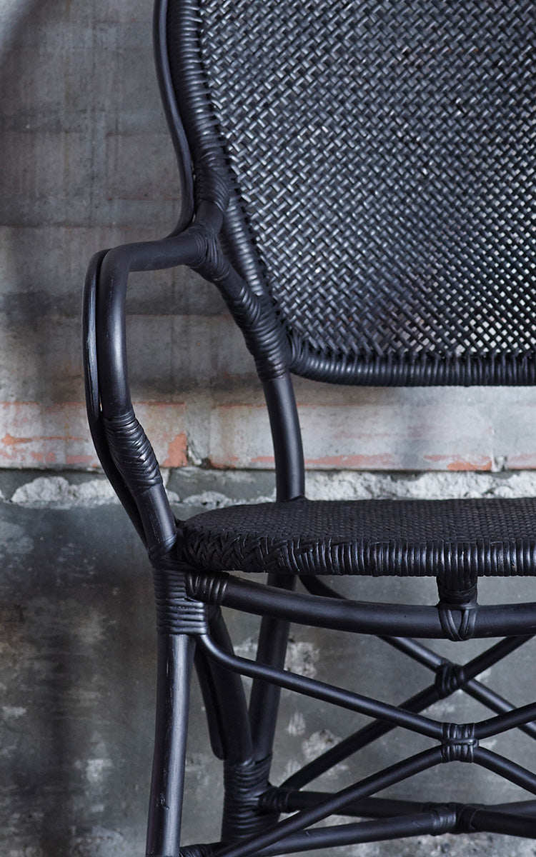 This is a close-up image of Rossini Armchair in black rattan. Detail of the all-black rattan weave and curved armrest.