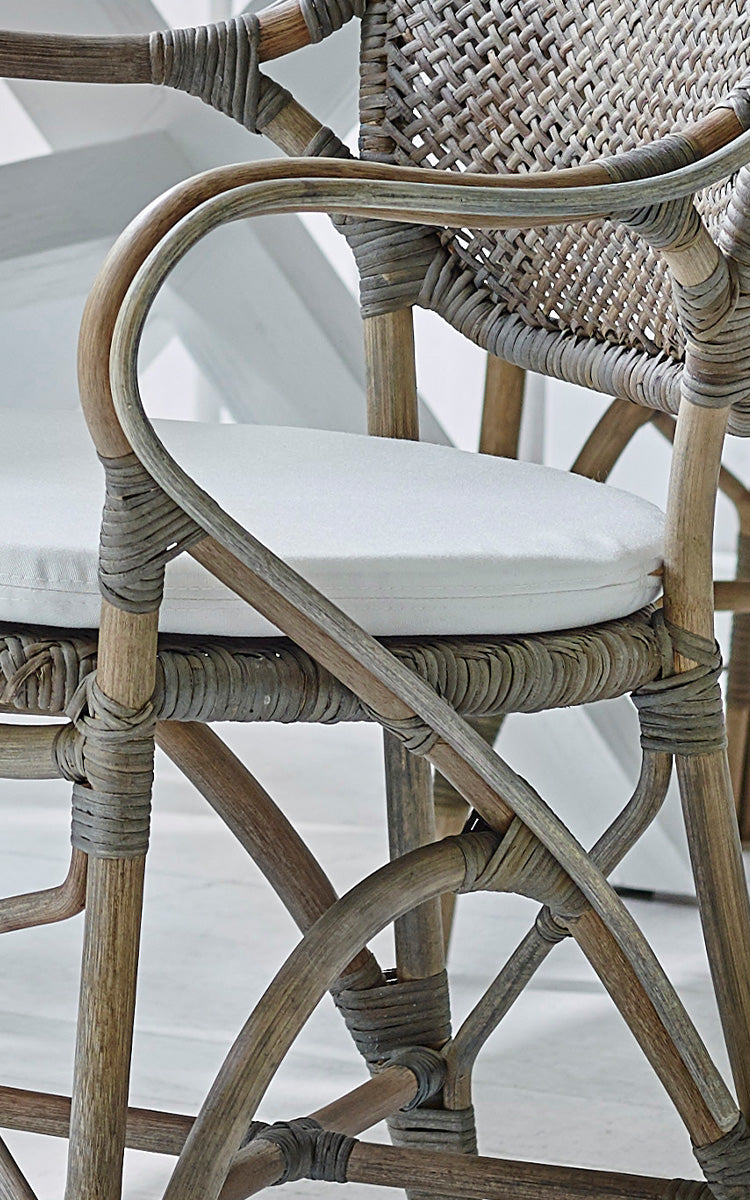 This is a close-up image of Rossini Armchair in taupe rattan. Detail of weathered taupe rattan with white seat cushion.