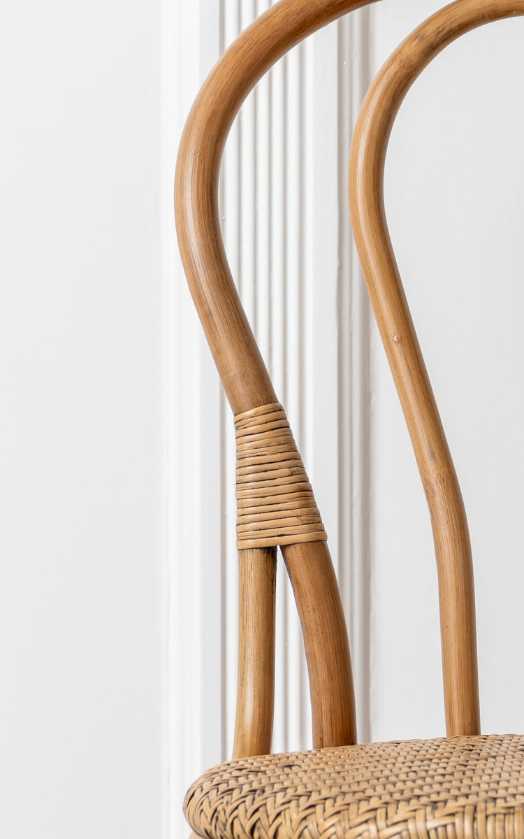 This is a close-up image of Lulu Dining Chair in antique rattan. The curved bentwood frame with rattan wrapping and woven seat highlight the design.