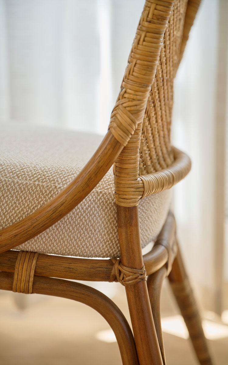 This is a close-up image of Melody Dining Chair in antique rattan. Cane backrest, cushioned seat and bound frame joints.