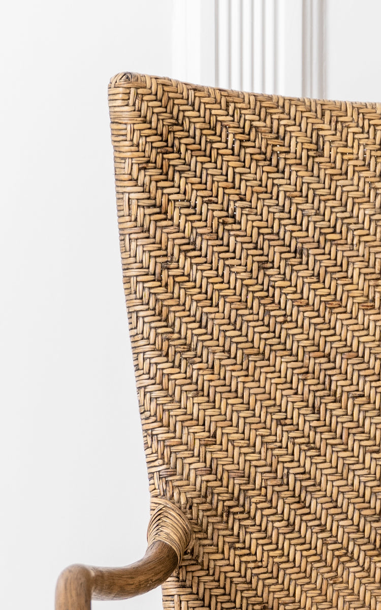 This is a close-up image of Melody Dining Armchair in antique rattan. Detail of the herringbone weave backrest and curved rattan armrest.