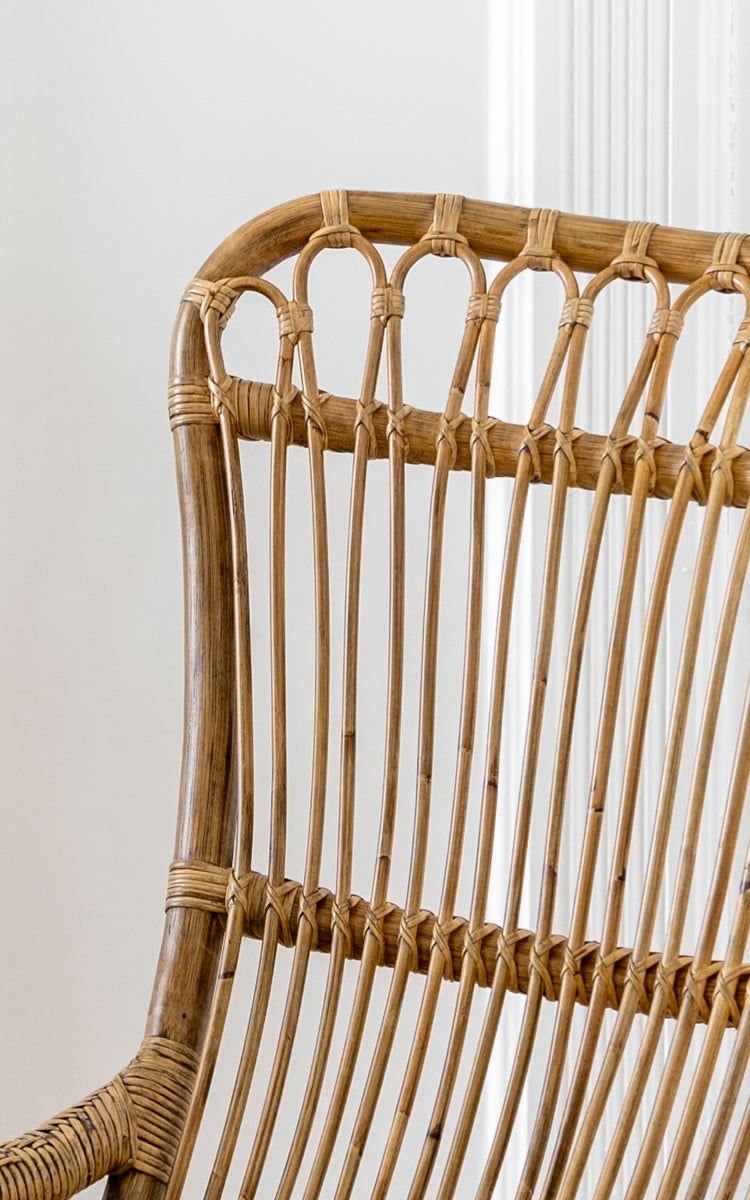 This is a close-up image of Monet Rocking Chair in antique rattan. Detail of the looped arch backrest and vertical rattan rod construction.