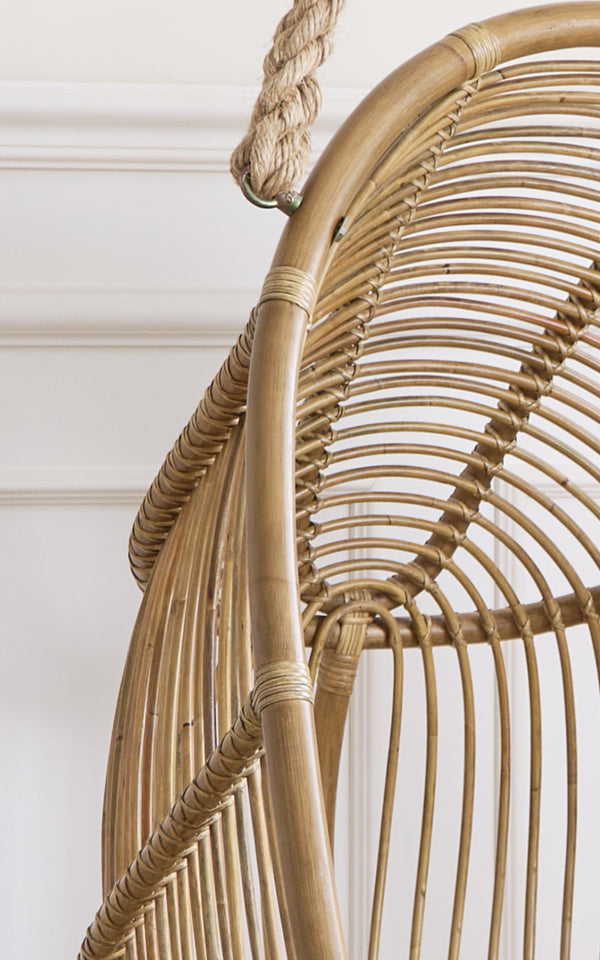 This is a close-up image of Renoir Hanging Chair in antique rattan. Detail of the curved rattan frame with radial spokes and rope hanger.