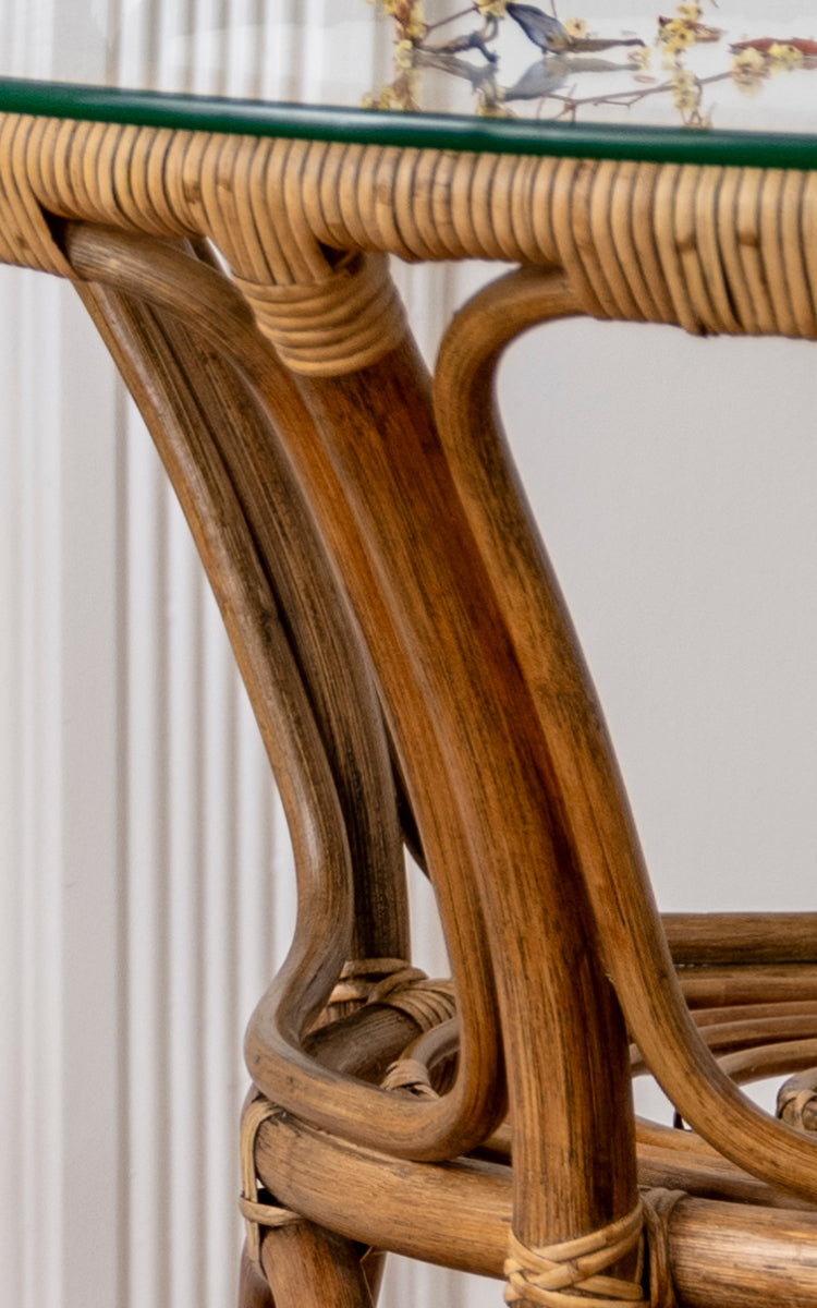This is a close-up image of Tony Café Table in antique rattan. Detail of the glass top edge, curved rattan frame and wrapped joints.