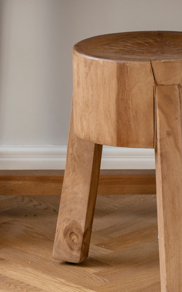 This is a close-up image of Roger Stool in teak indoor. Detail of the solid teak seat and three chunky angled legs.