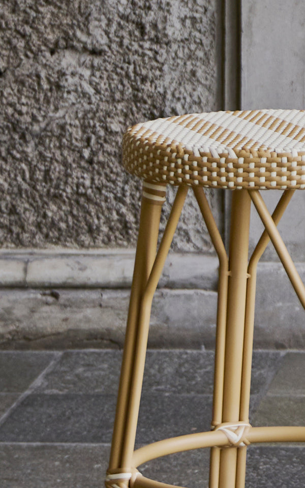 This is a close-up image of Simone Stool in striped honey ivory ArtFibre Skin on Rattan frame. Seat detail against a rough stone wall.