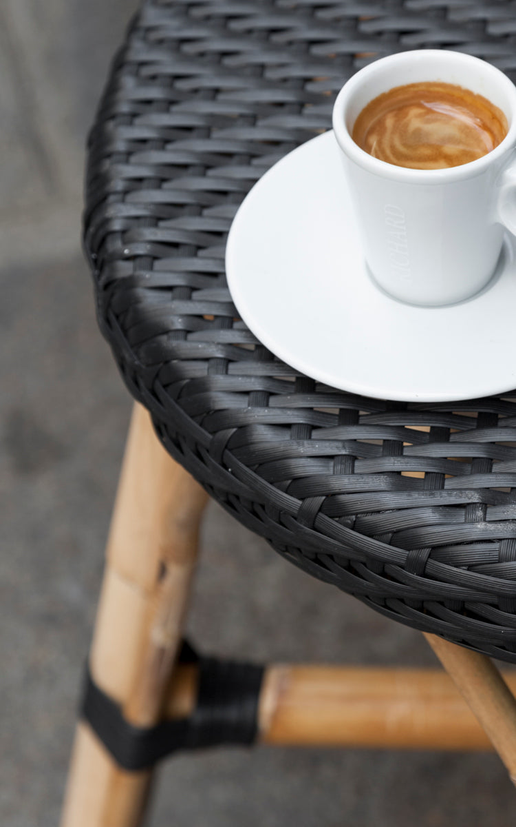 This is a close-up image of Simone Counter Stool in black ArtFibre Skin on Rattan frame. Detail of the woven seat with an espresso cup on top.