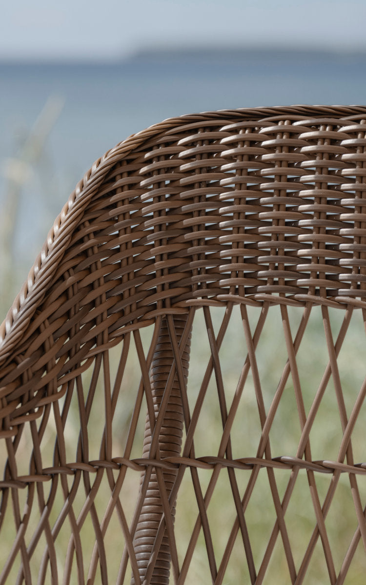 This is a close-up image of Charlot 3-Seater Exterior Sofa in brown artfibre aluminum. Open weave backrest against a sea view.