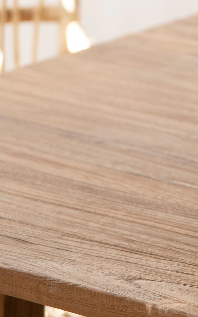 This is a close-up image of Lucas Teak Dining Table 240X100 cm in teak indoor. The natural wood grain of the solid teak tabletop is highlighted.