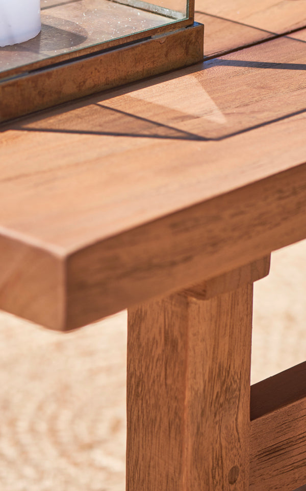 This is a close-up image of Julian Teak Lounge Table 140x55 cm in teak outdoor. The thick solid teak edge and robust leg joints are shown.
