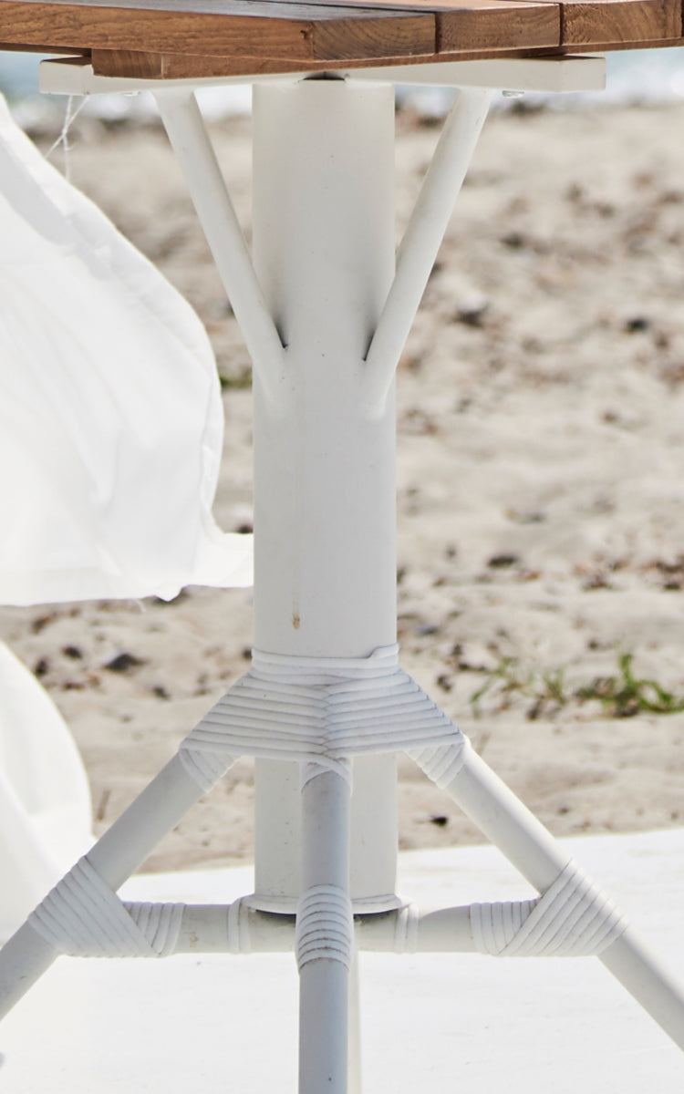 This is a close-up image of Nicole Cáfe Table Teak 70x70 cm in white aluminium frame white artfibre.