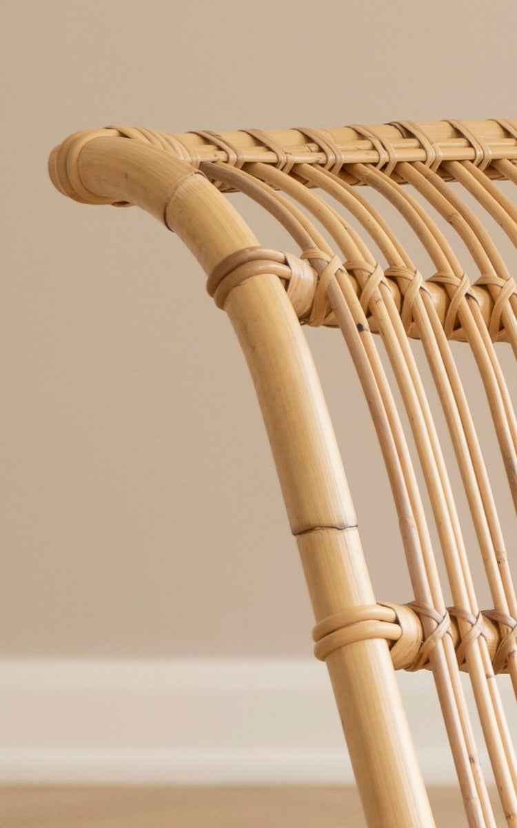 This is a close-up image of Paris Lounge Chair in polished natural rattan. Detail of the curved rattan frame and arched seat slats.