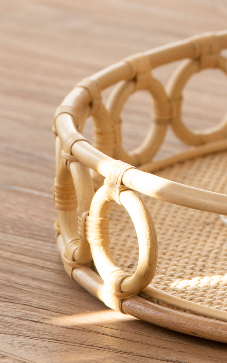 This is a close-up image of Mira Tray in natural rattan. Detail of the circular ring border and woven cane base of the round tray.