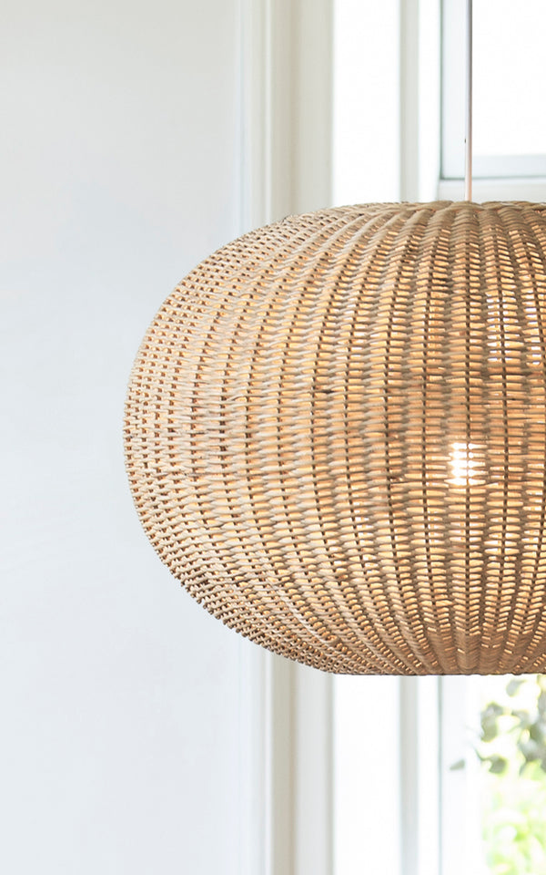 This is a close-up image of Tangelo Lampshade Ø62 cm | Large in natural rattan. Detail of the large rattan weave of the rounded pendant by a window.