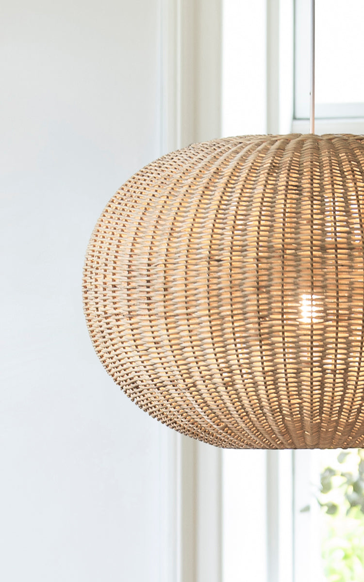 This is a close-up image of Tangelo Lampshade Ø62 cm | Large in natural rattan. Detail of the large rattan weave of the rounded pendant by a window.